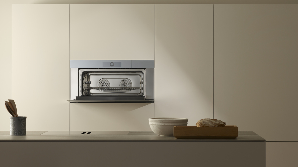 Moderne, minimalistische Küche mit Edelstahlofen, grauen Utensilienbehälter und rustikalem Brotkasten.