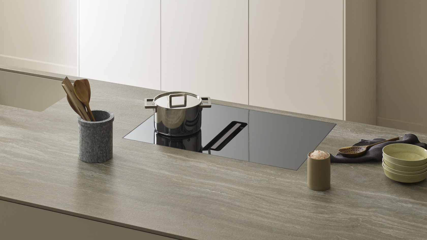 Moderne Küche mit Induktionskochfeld, Edelstahltopf, Holzutensilien und gestapelten grünen Schalen.