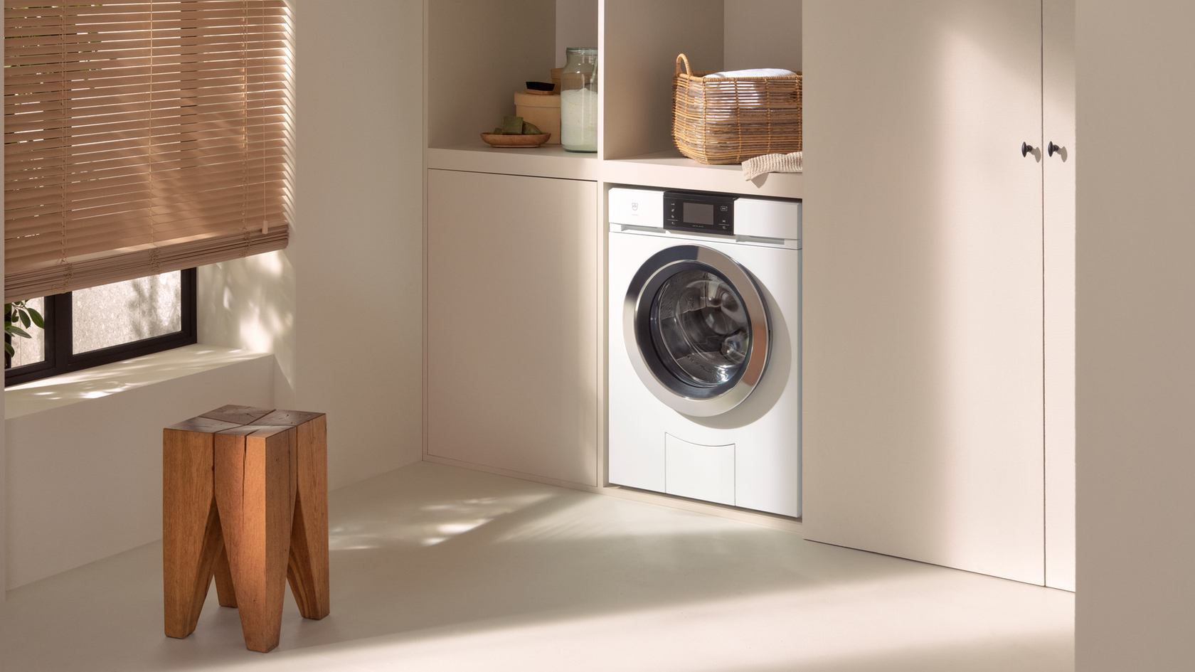 Moderner Waschraum mit integrierter Waschmaschine, hölzernem Hocker und Korb auf Schrank.