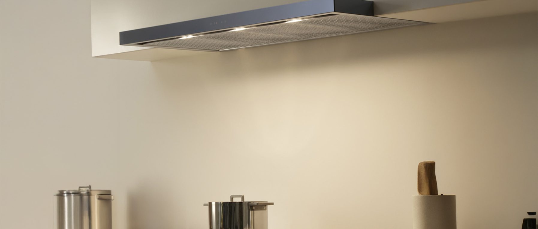 Moderne Küche mit Dunstabzugshaube, beleuchtetem Edelstahltopf und Küchenrollenhalter.