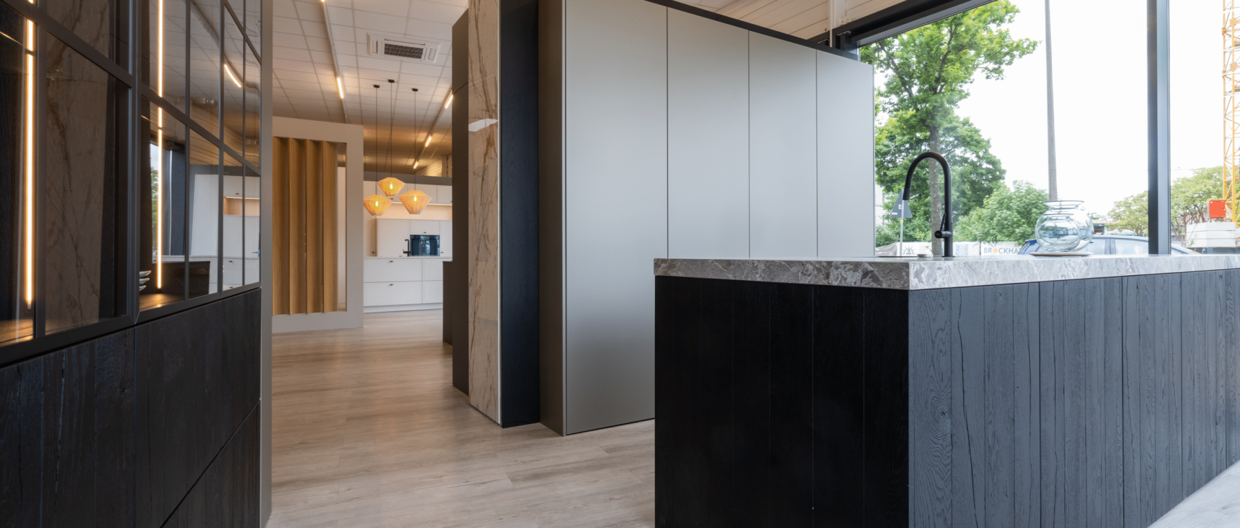 Moderner Küchenbereich mit dunkler Holzinsel, Marmorplatte, warmem Licht und großen Fenstern.