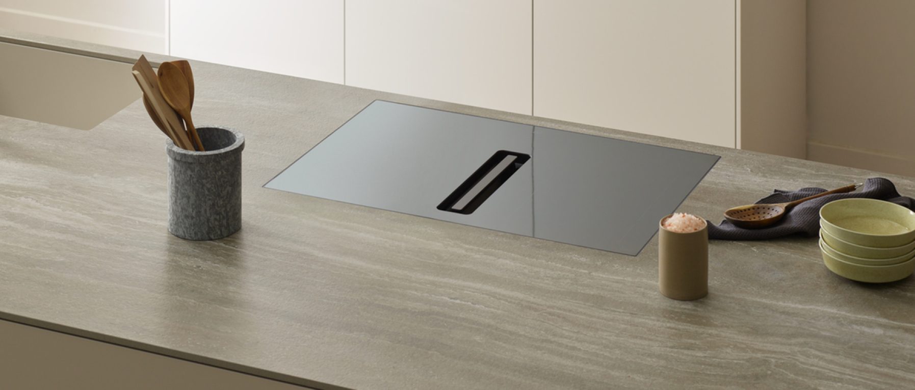 Moderne Küche mit grauer Arbeitsplatte, schwarzer Kochfläche, grünen Tellern und Holzutensilien.