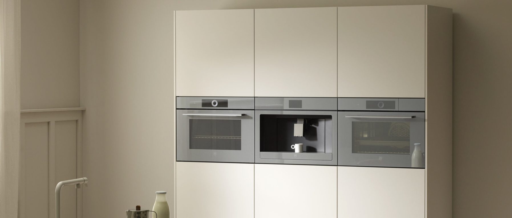 Moderne Küche mit zwei grauen Öfen und einer Kaffeemaschine, umgeben von hellbeigen Schränken.