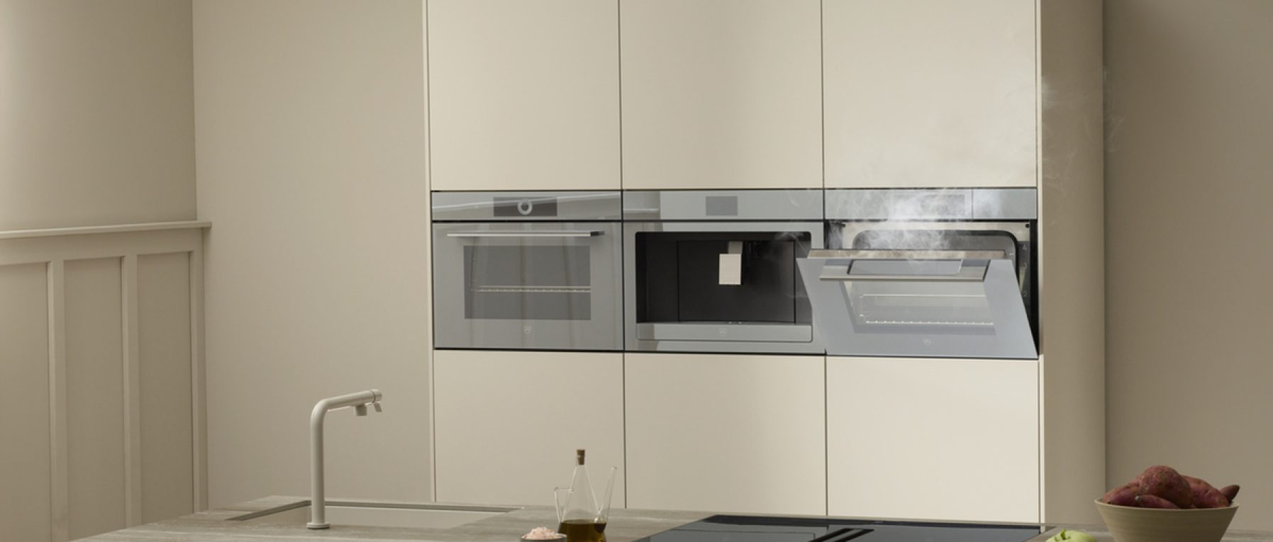 Moderne Küche mit Dampfgarer in Betrieb, roten Kartoffeln, grünem Apfel und Ölflasche auf Arbeitsplatte.