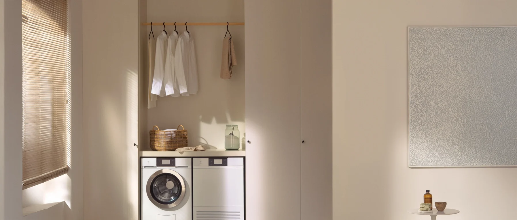 Ein minimalistischer Waschraum mit Waschmaschine, Trockner, Regal und neutralen Farbtönen.